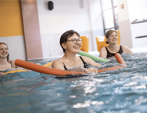 Frau im Wasser mit Poolnudel bei Aquagymnastik
